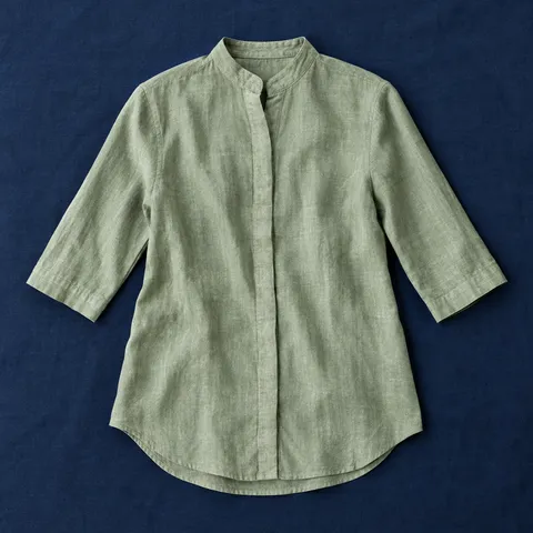 Camisa cuello mao Algezares en verde salvia, prenda extendida sobre mantel azul